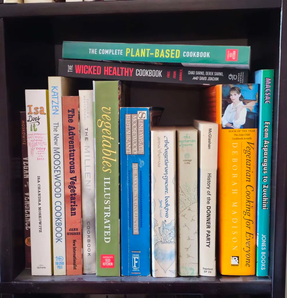 a bookshelf with a bunch of vegetarian cookbooks and one that isn't. (it's called _History of the Donner Party_)